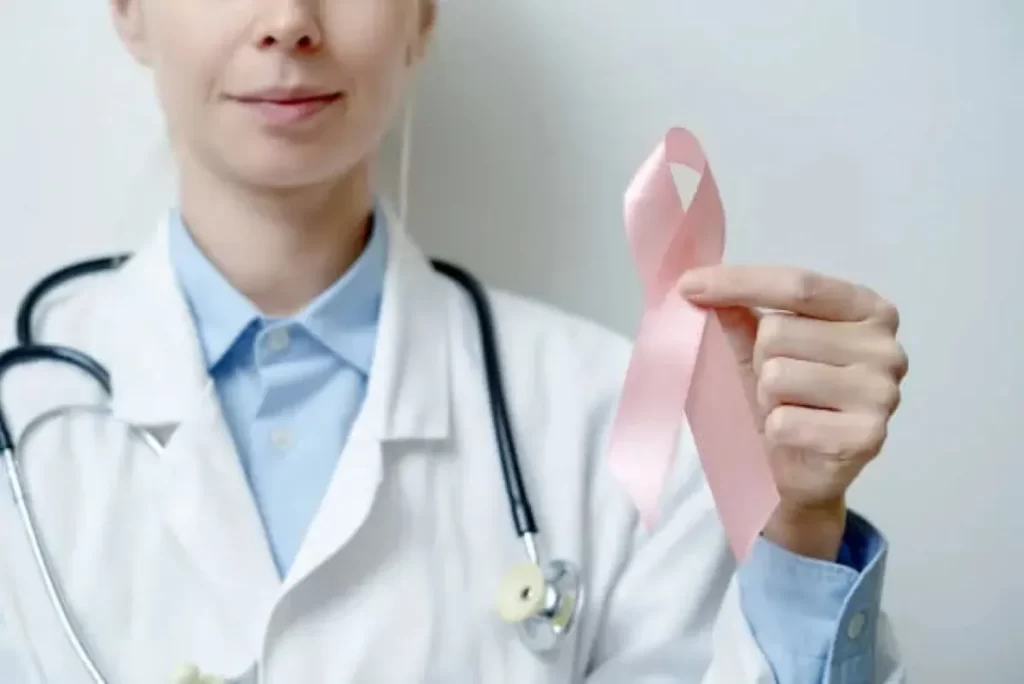 白衣を着た女性医師が左手にピンクリボンを掲げ、乳がん啓発を象徴するポートレート