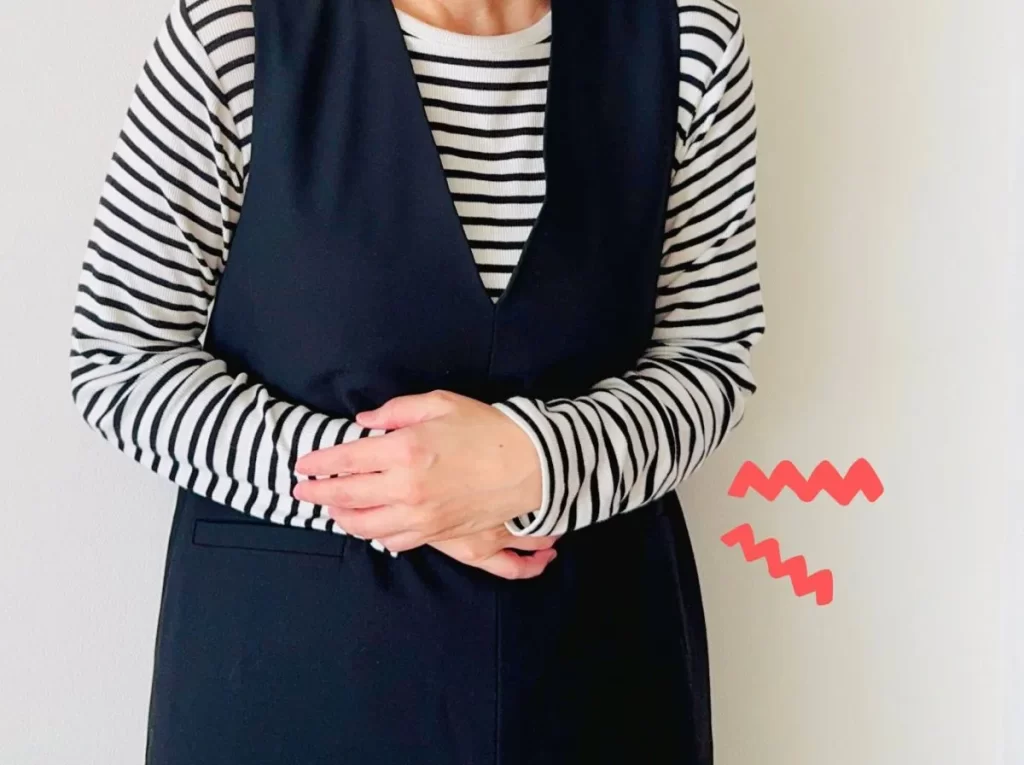生理痛で辛そうにお腹を抱える女性 シマシマ長袖と紺色カーディガン着用