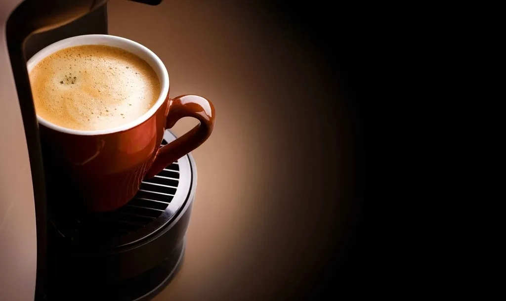 赤いカップに注がれたコーヒー。コーヒーマシンから注がれている様子で、背景は黒