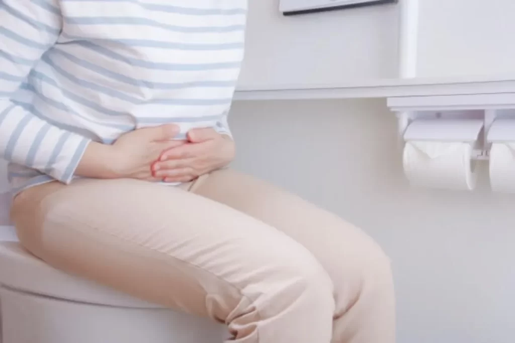 トイレの便座に座り、お腹を抱えて痛そうにする女性のクローズアップ