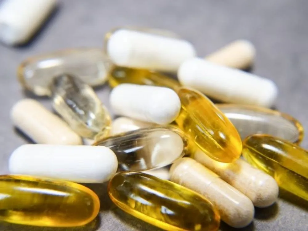 散らばった黄色・白・透明のサプリメント錠剤、過剰摂取による尿路結石リスクを象徴