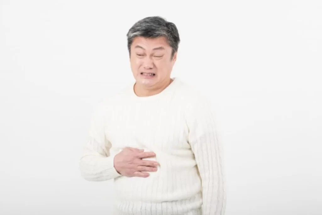クローン病の腹痛で苦しむ男性。お腹を右手で押さえ、辛い表情を浮かべている様子