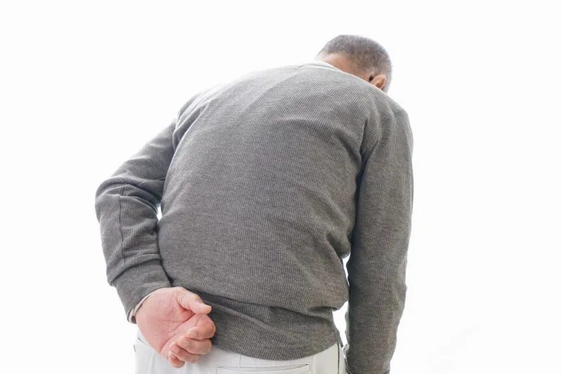 腰とお尻の痛みを抱えるシニア男性が左手で腰を押さえている後ろ姿。
