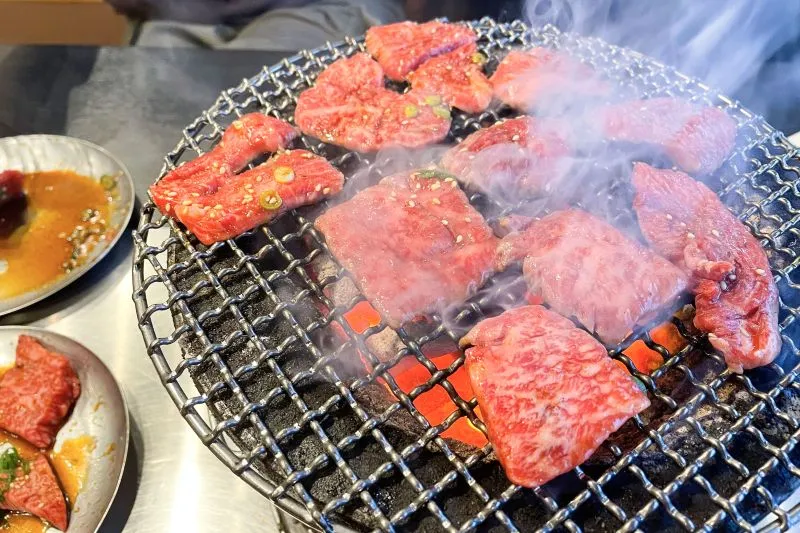 七輪で焼かれる焼肉と立ち上る煙のクローズアップ