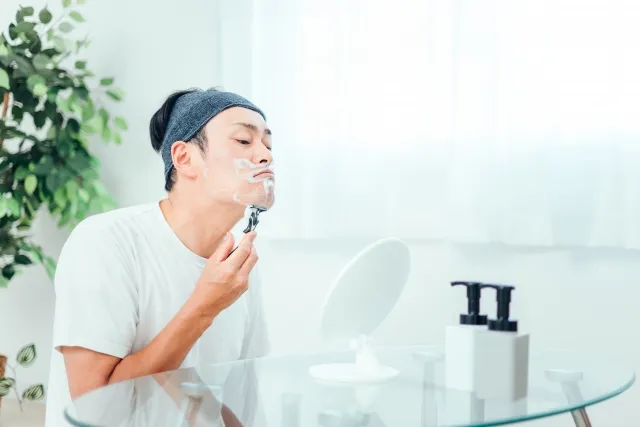 鏡に向かってひげを剃る白い半袖の男性。中医学で精子生成と老廃物排出の関係を示す象徴的な場面。