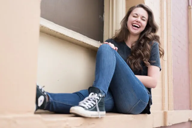 屋外で窓辺に座りお腹を抱えて大笑いする白人女性