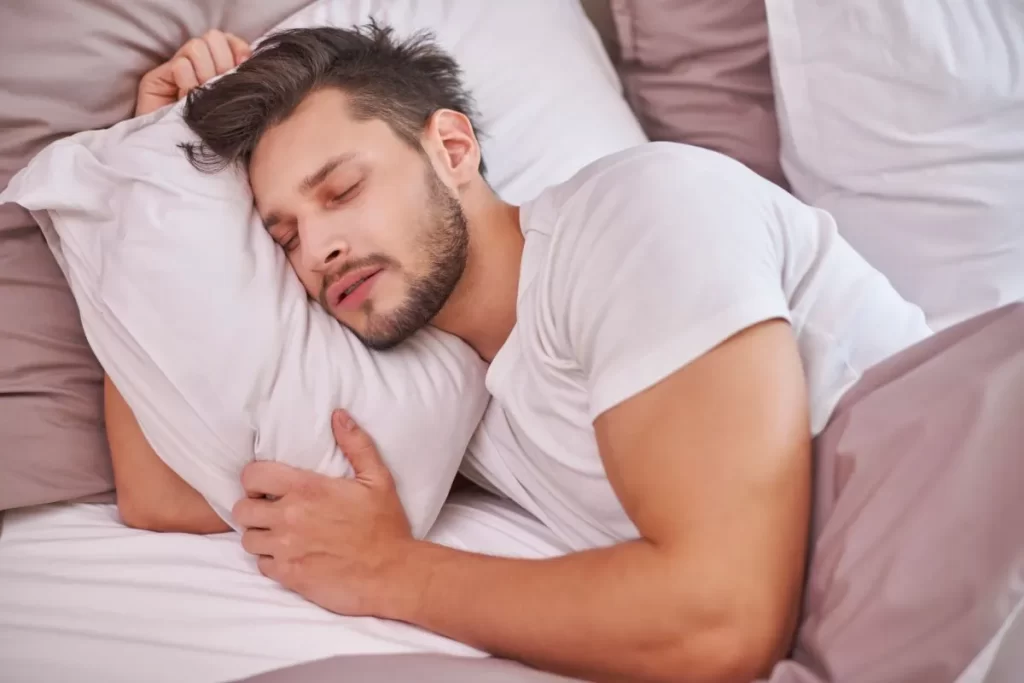 白い寝具で横になり、深く眠っているヒゲの白人男性。睡眠の改善と体調回復をイメージした写真。