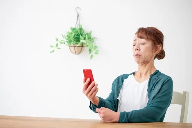 緑のカーディガンを着た高齢女性が右手にスマホを持って遠くに離してみる様子。視力低下や視野欠損の症状をイメージしたアイキャッチ画像。