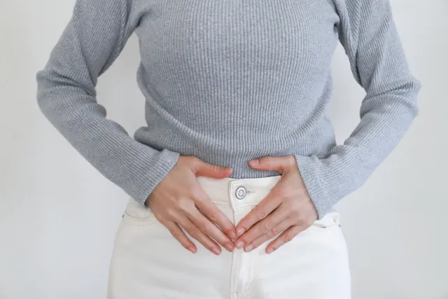 乳がん手術後に便秘が続き、お腹が張って苦しむ50歳女性。両手でお腹を抱える様子。漢方治療で1週間で便通が改善した症例を表す画像。