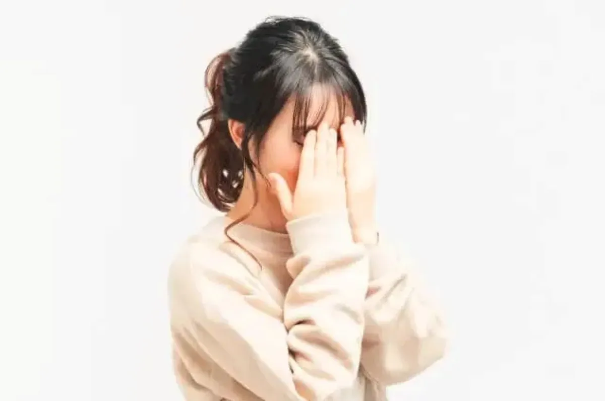 米色のセーターを着た女性が、運動後に顔だけ汗が出ず真っ赤になり、恥ずかしそうに両手で顔を隠しているイラスト