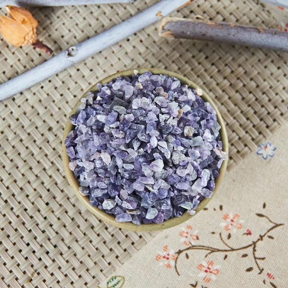 漢方薬の鉱物生薬・紫石英を白い容器に入れた様子。隣に2本の木の枝、下に梅の花が刺繍された布が置かれている