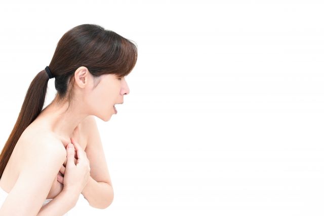 白い背景に、月経随伴性気胸による胸の痛みで苦しそうに両手で胸を抑える女性。足つぼ整体で症状改善の可能性