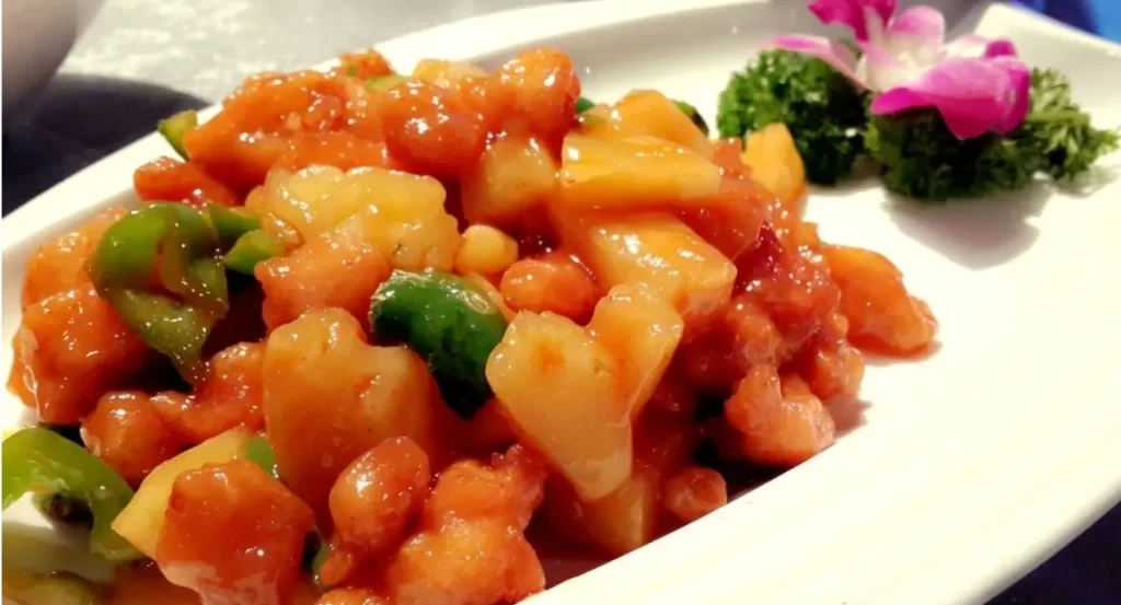 白い皿に盛られた酢豚、背景に緑の野菜とピンクの花 - 逆流性食道炎改善後の食欲回復の象徴