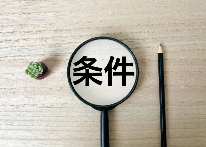 拡大鏡で「条件」の文字を示し、鉛筆と緑の葉が置かれた上からの写真