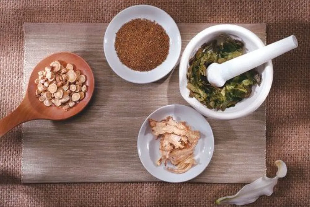 木の板に並べられた漢方生薬、白い容器3つと大きな木のスプーンで生薬をすくう様子、伝統中国医学の煎じ薬材料