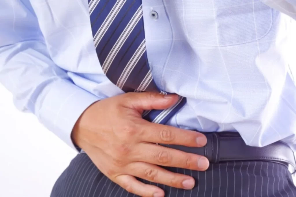 激しい腹痛で前屈みになり、お腹を押さえるサラリーマン