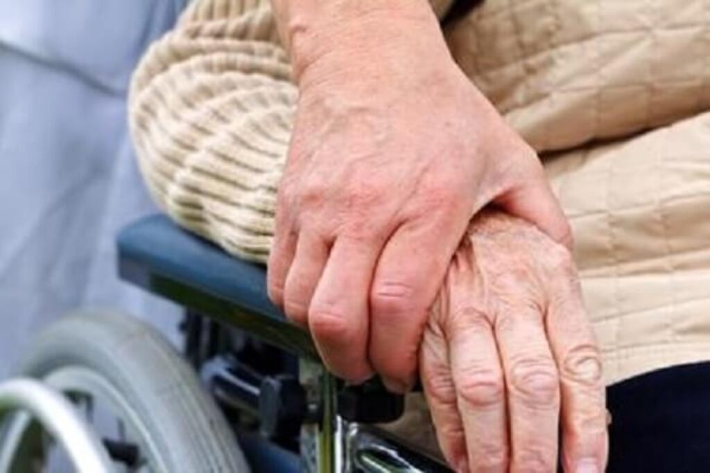 車椅子に座る高齢者の手を優しく抑える手