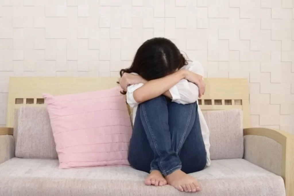 告知のショックでソファーで膝に頭をうずめて悲しむ女性