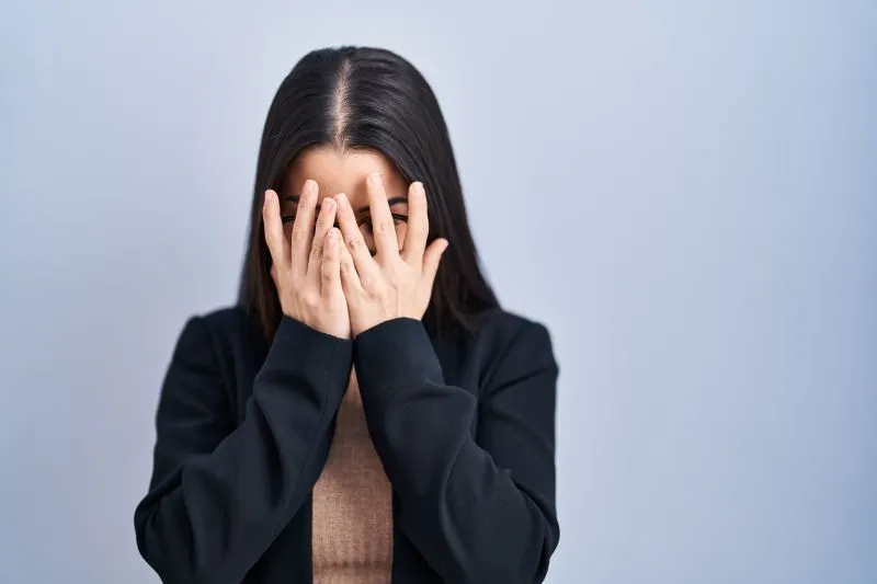 恐怖で顔を手で覆い、指の間から目を出している女性の写真