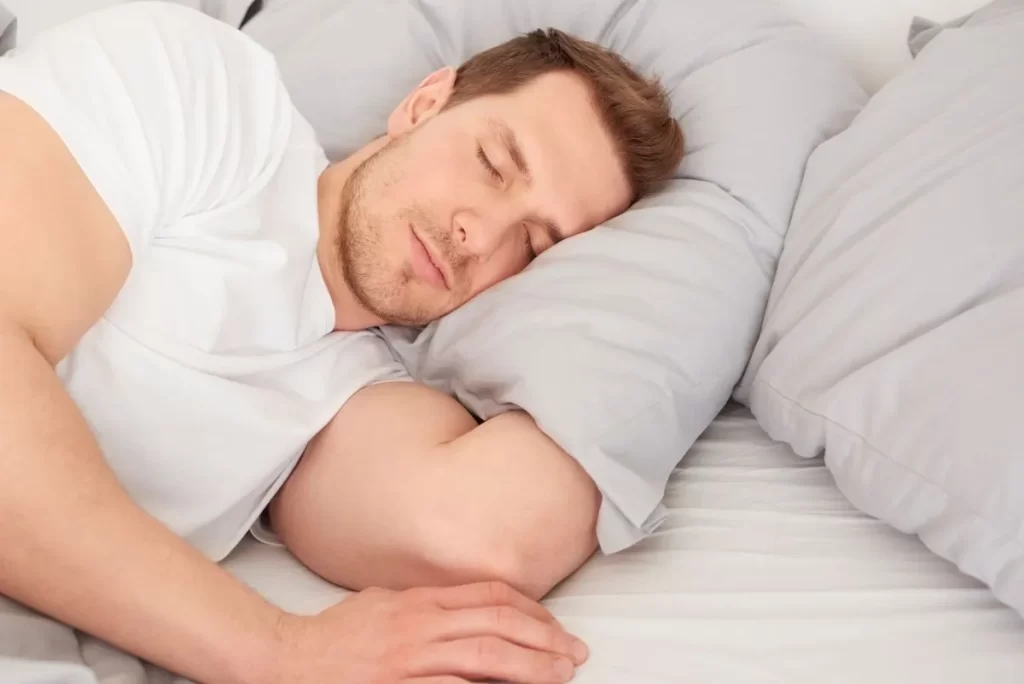 白い寝具で横になり、気持ち良さそうに眠っている白人男性の写真