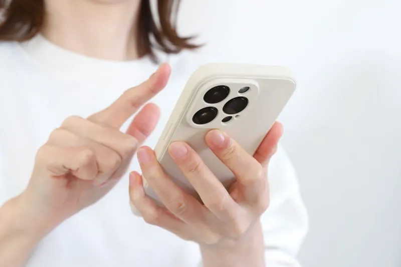 スマホを左手に持ち、右手の指で操作する女性の手元のクローズアップ。長時間のスマホ使用による目の疲れをイメージした写真。
