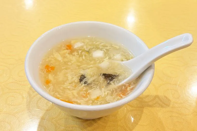 黄色いテーブルの上に置かれた白い茶碗とスプーン、中に入った温かい卵スープ。
