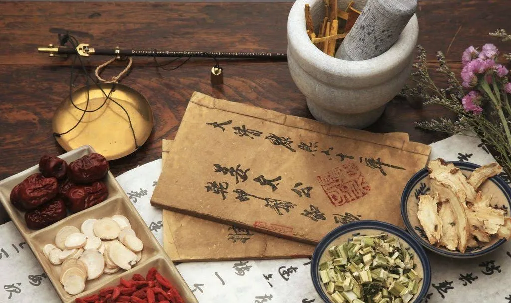 漢方生薬と秤、古本、花が並ぶ中医学の治療風景
