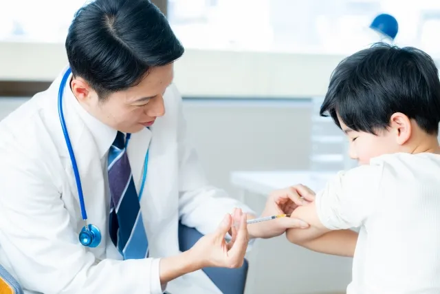 白衣の医師が子供の腕にワクチン接種をしている様子。