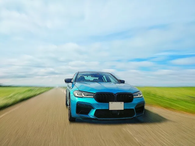 BMW M5スポーツカーが緑の畑沿いを高速走行するダイナミックな写真