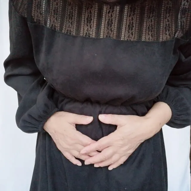 黒いワンピースを着た女性がお腹の痛みで両手で抱え、苦しむ様子。潰瘍性大腸炎や便秘の症状を象徴するイラスト。