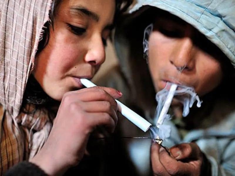 ヘロインを吸引している若者（パーカー姿の男女）。白い煙を吐きながら薬物使用の様子