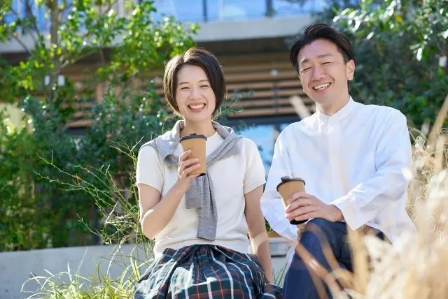 笑顔のカップルが芝生に座ってお茶を飲みながら楽しげに話す様子