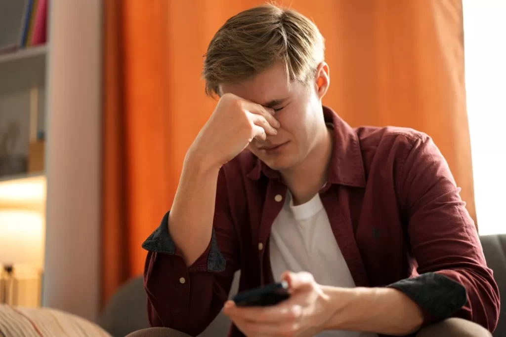 スマホを持ちながら涙目で顔を押さえる若い男性