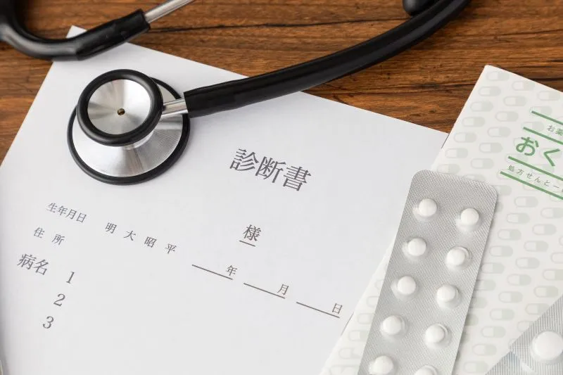 診断書、薬のシート、薬袋、聴診器が並べられた医療関連の写真