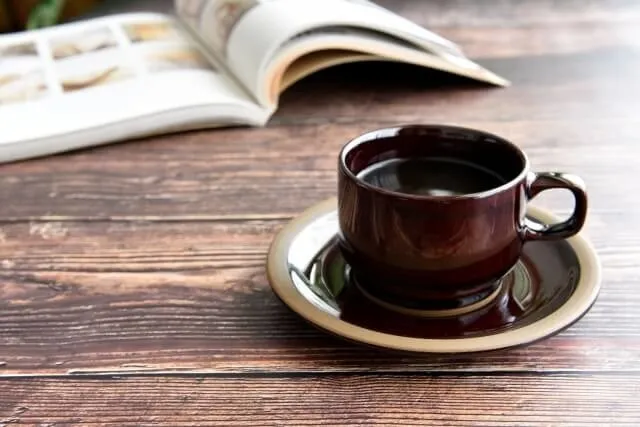 木製テーブルに置かれたコーヒーカップと開いた本、背景に柔らかい光