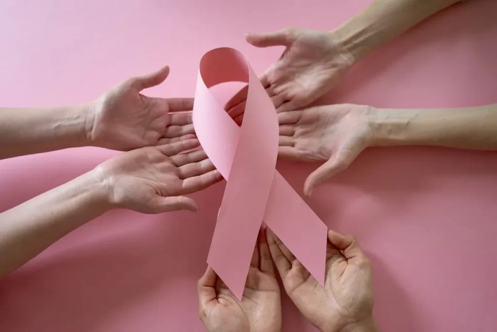 複数の手がピンクのリボンを支えて支え合う様子、乳がん啓発とサポートを象徴