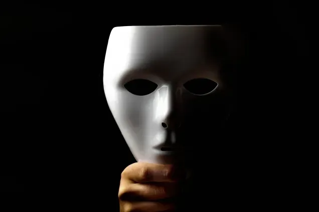 黒背景で白い仮面を手に持つ人物のクローズアップ写真
