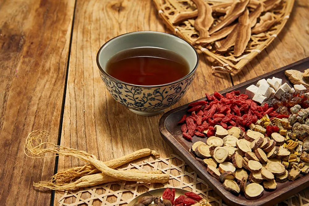 木の机に並ぶ漢方素材と花柄の茶碗に入った漢方薬の汁