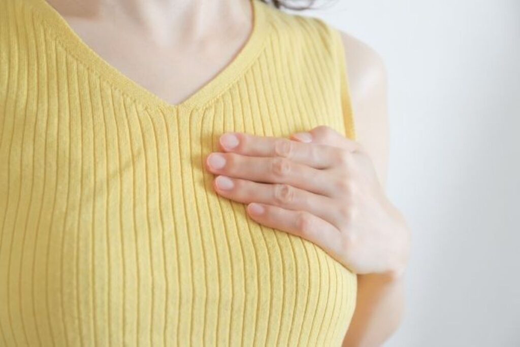 黄色いタンクトップの女性が左胸を手で触れてセルフチェックしている様子のクローズアップ