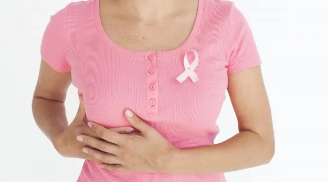 ピンクの半袖を着た女性が胸を両手で触り、乳がんを気にしている様子