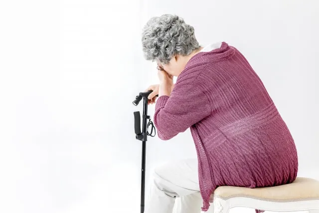 低用量アスピリン長期服用後に脳卒中になり左半身不随で苦しむ女性　杖をついておでこを押さえる