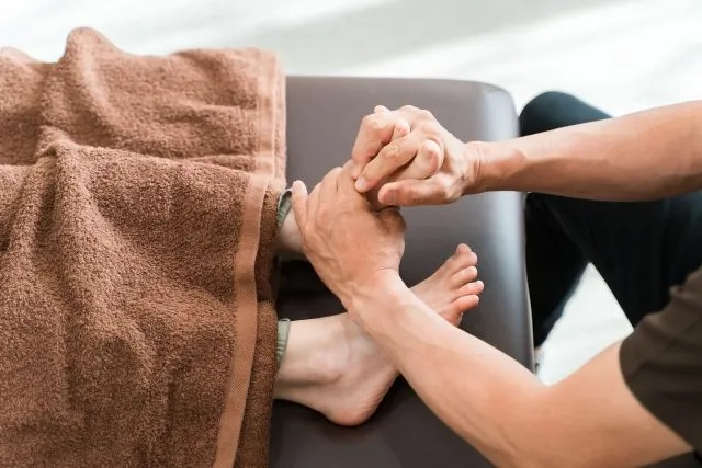 男性マッサージ師が足つぼ整体で足裏を力強く揉む様子。パニック障害と冷え性の改善をサポートする施術シーン。
