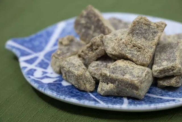 青い皿に乗せた黒糖生姜の塊のクローズアップ。パニック障害と冷え性改善に役立つ自然療法の食材。