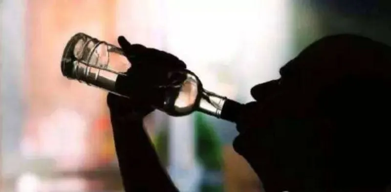 お酒の瓶を持ち、顔を上げて一気飲みする人物のシルエット