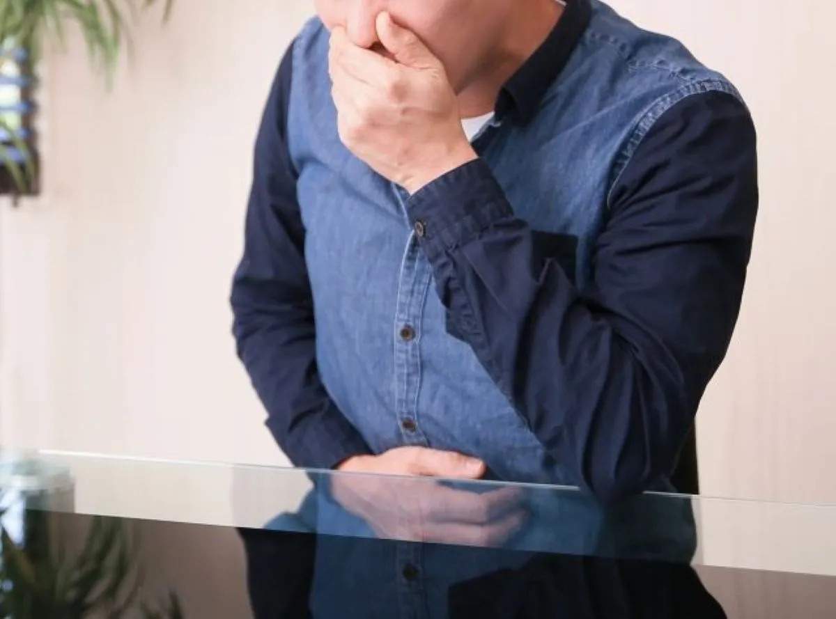 胃酸逆流で苦しむ男性 お腹を押さえ吐き気を我慢する様子
