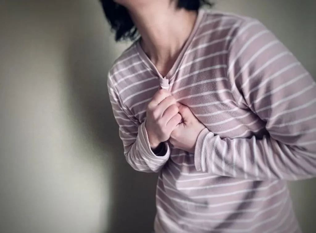 胸の痛みや動悸に苦しむ女性の胸元のクローズアップ写真（暗い背景）