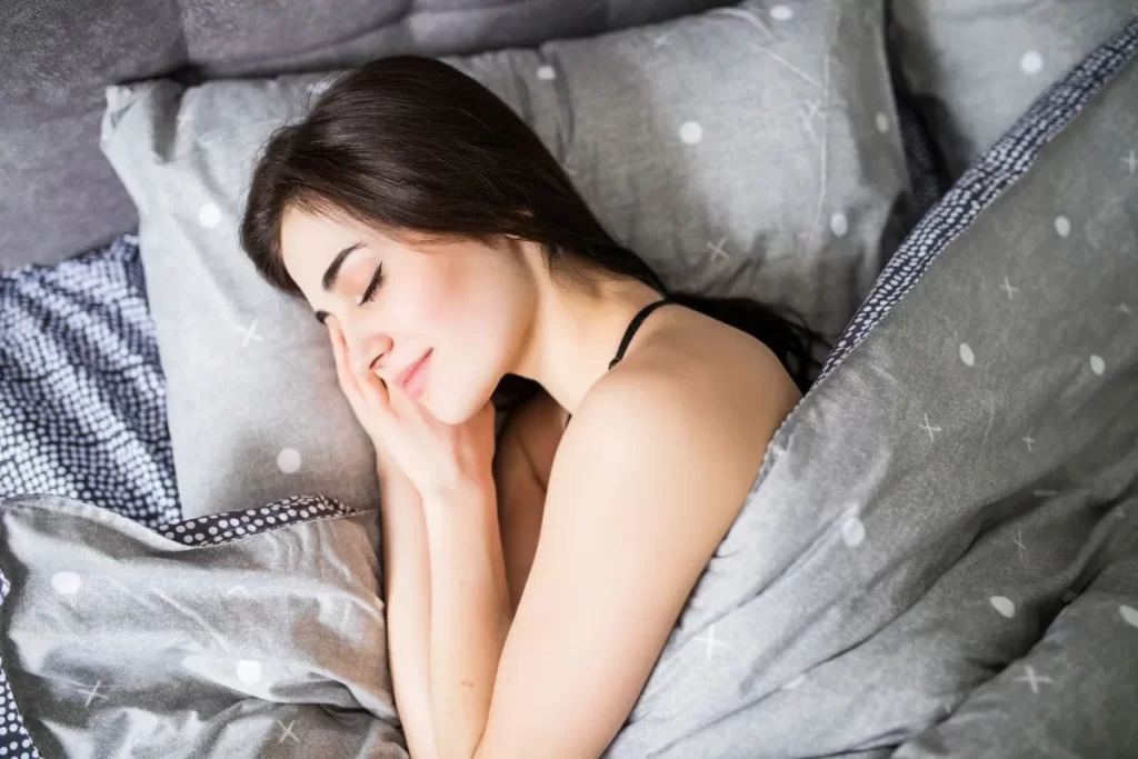 布団の中で微笑みながら眠る女性。体が温まり、睡眠の質が改善した様子を表すイメージ