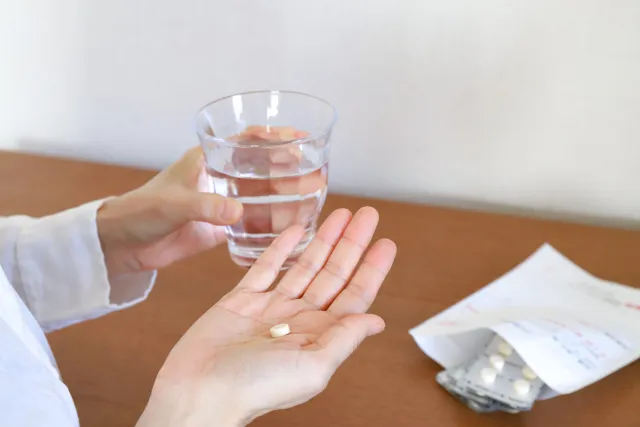 薬を手に持ち、水で飲もうとしている女性の手元の写真