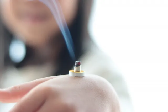 笑顔の子どもが手の甲に千年灸を乗せてお灸をしている様子 煙が出ているクローズアップ