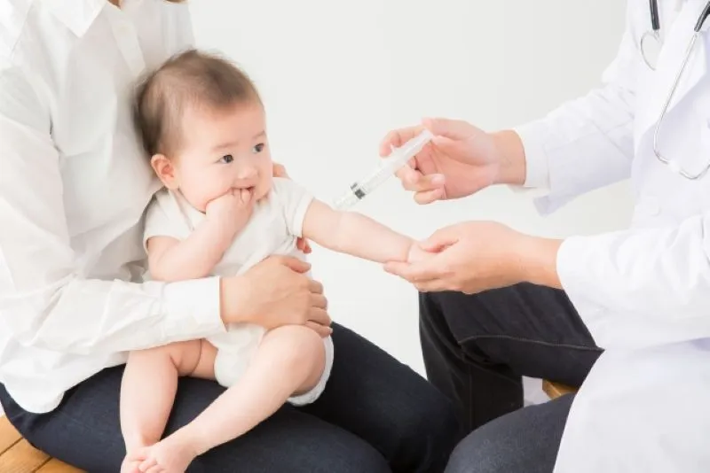 白衣の医師が赤ちゃんの腕にワクチン注射をしている場面